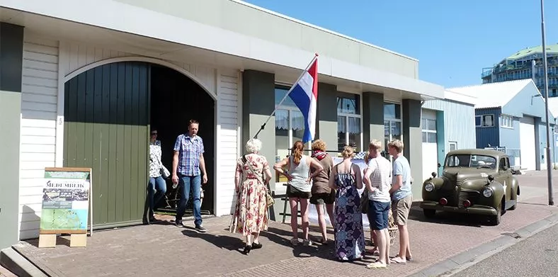 Bezoekers lopen naar de ingang van een museum over de Tweede Wereldoorlog waar legerauto’s voorstaan