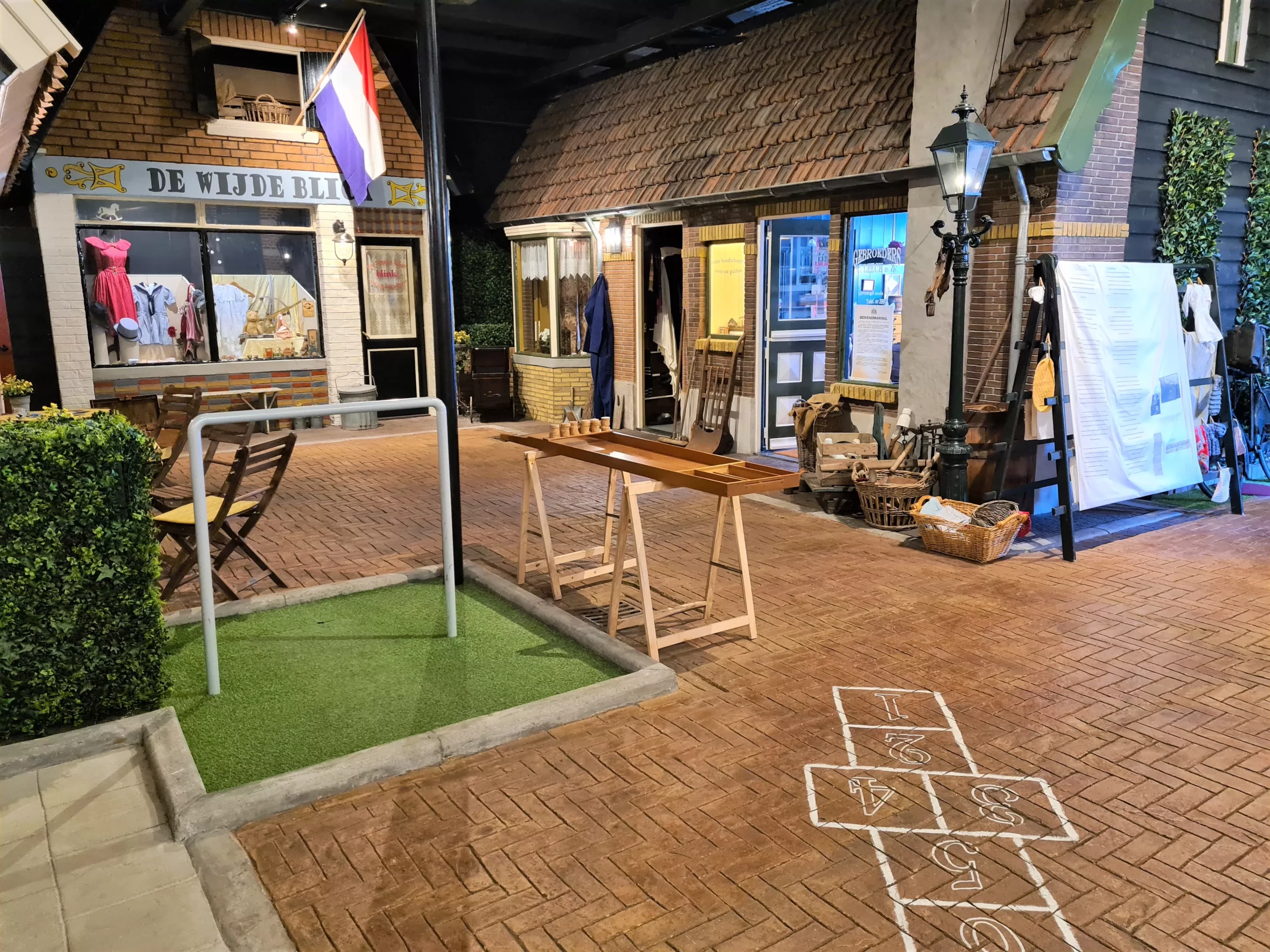 Mooi dorpspleintje met hink-stap-sprong, klimrek en winkeltjes in een overdekt museum over de Tweede Wereldoorlog
