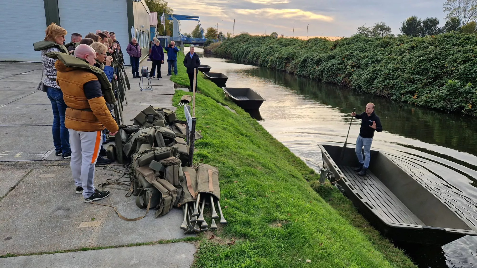 Een groep krijgt van de spelleider uitleg over de activiteiten die ze met elkaar buiten gaan doen zoals een wedstrijd in boten op het water